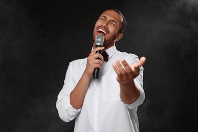 Photo of Handsome man with microphone singing on black background