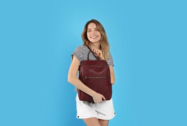 Happy woman with backpack on light blue background