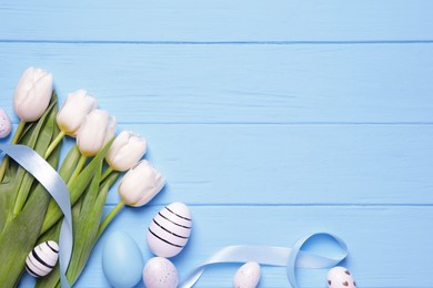 Flat lay composition of painted Easter eggs and tulip flowers on light blue wooden table. Space for text