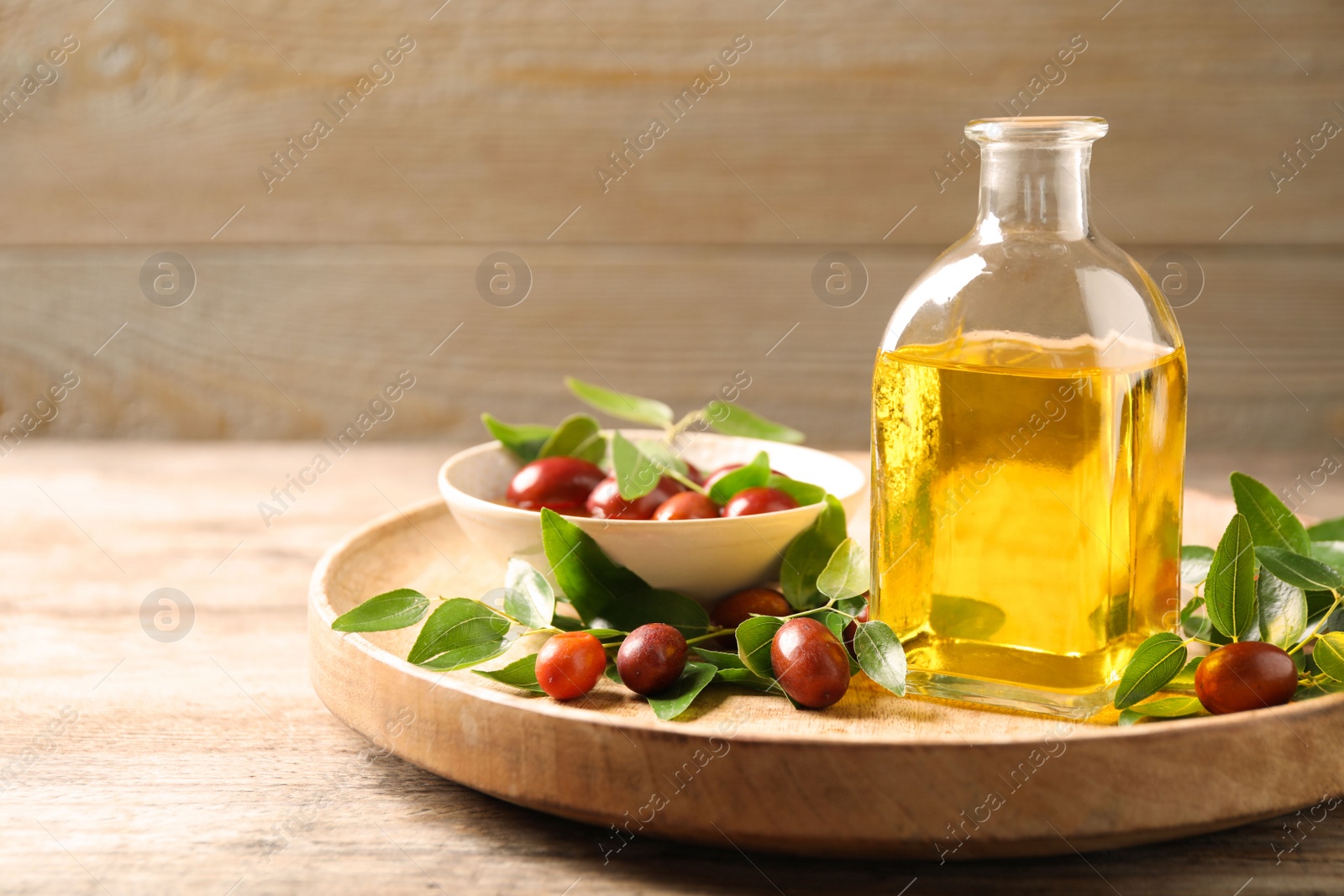 Photo of Glass bottle with jojoba oil and seeds on wooden table. Space for text