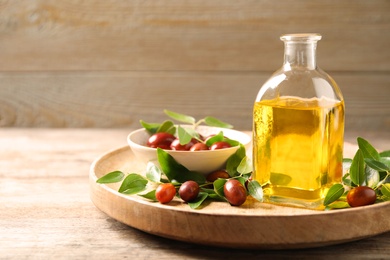 Glass bottle with jojoba oil and seeds on wooden table. Space for text