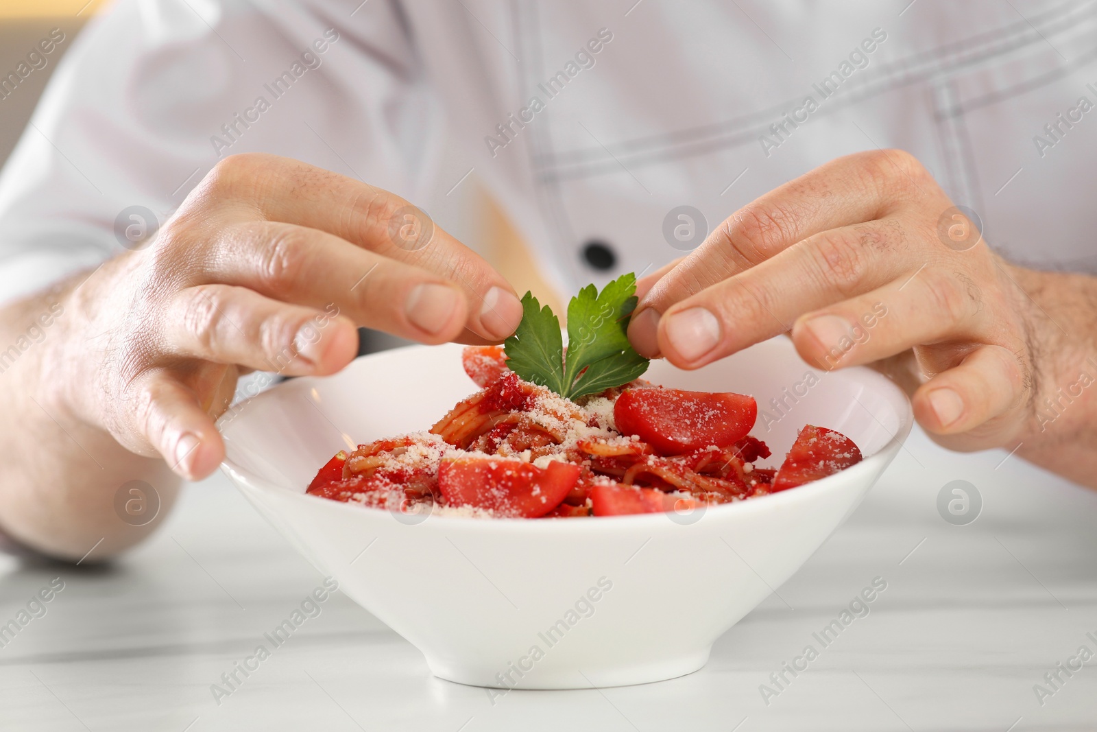 Photo of Professional chef decorating delicious spaghetti with parsley at marble table, closeup