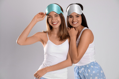 Photo of Beautiful women wearing sleeping masks on light grey background. Bedtime