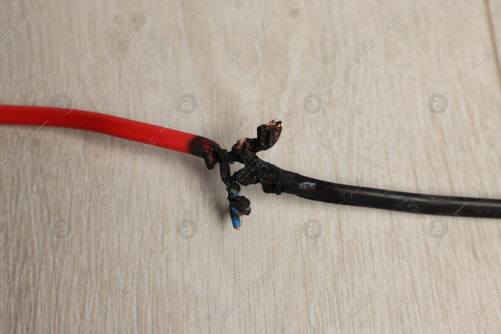 Photo of Burnt red wire on wooden floor, closeup. Electrical short circuit