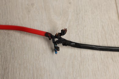 Photo of Burnt red wire on wooden floor, closeup. Electrical short circuit