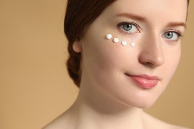 Photo of Beautiful woman with freckles and cream on her face against beige background, closeup