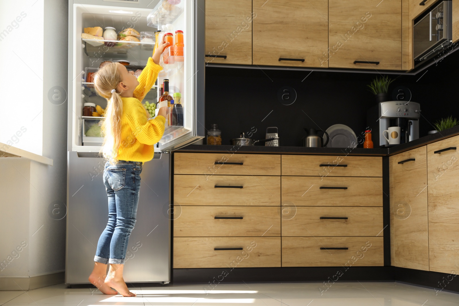 Photo of Girl taking bottle with juice out of refrigerator in kitchen