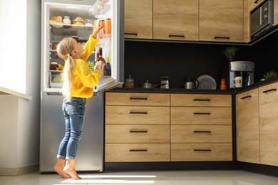 Photo of Girl taking bottle with juice out of refrigerator in kitchen