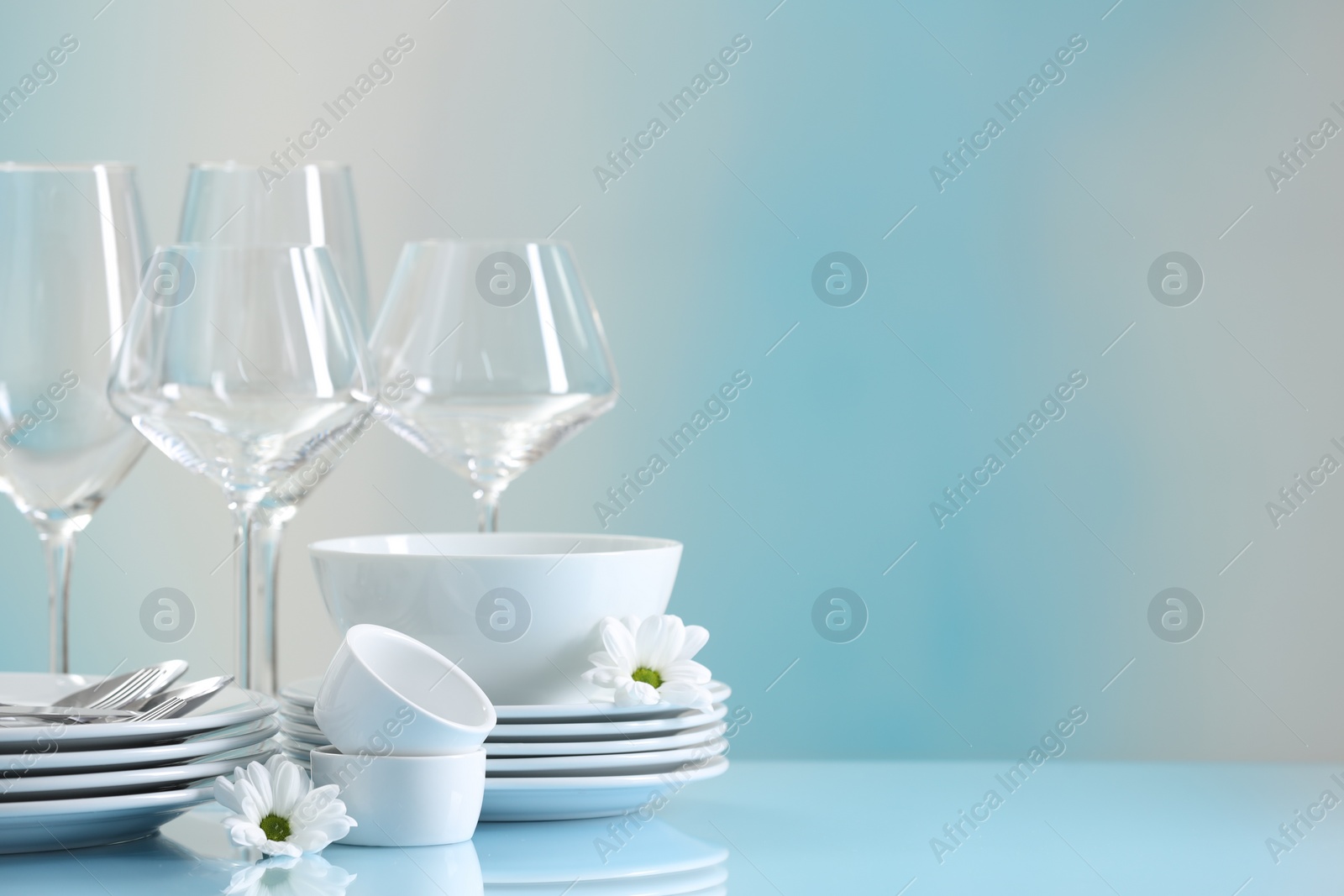 Photo of Set of many clean dishware, cutlery, flowers and glasses on light blue table. Space for text