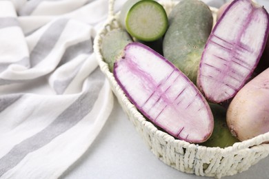 Photo of Purple and green daikon radishes in wicker basket on light grey table, closeup