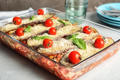 Photo of Baked eggplant with tomatoes, cheese and basil in dishware on table