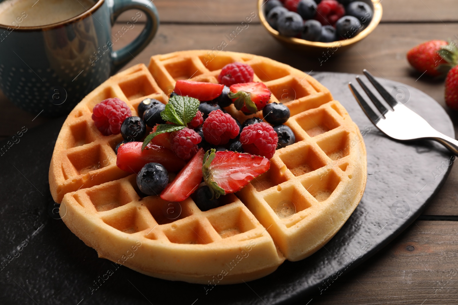 Photo of Tasty Belgian waffle with fresh berries served on wooden table, closeup