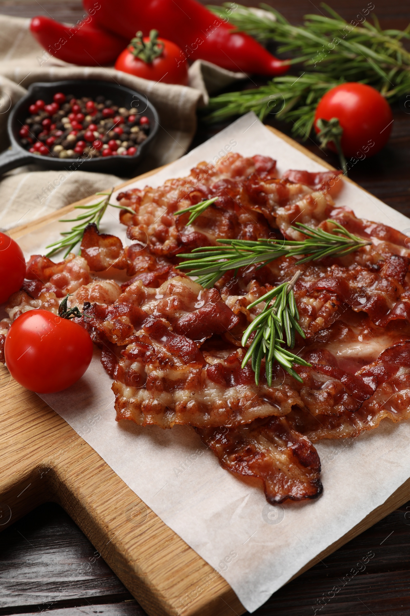 Photo of Slices of tasty fried bacon, rosemary, tomatoes and peppercorns on wooden table