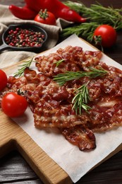 Photo of Slices of tasty fried bacon, rosemary, tomatoes and peppercorns on wooden table