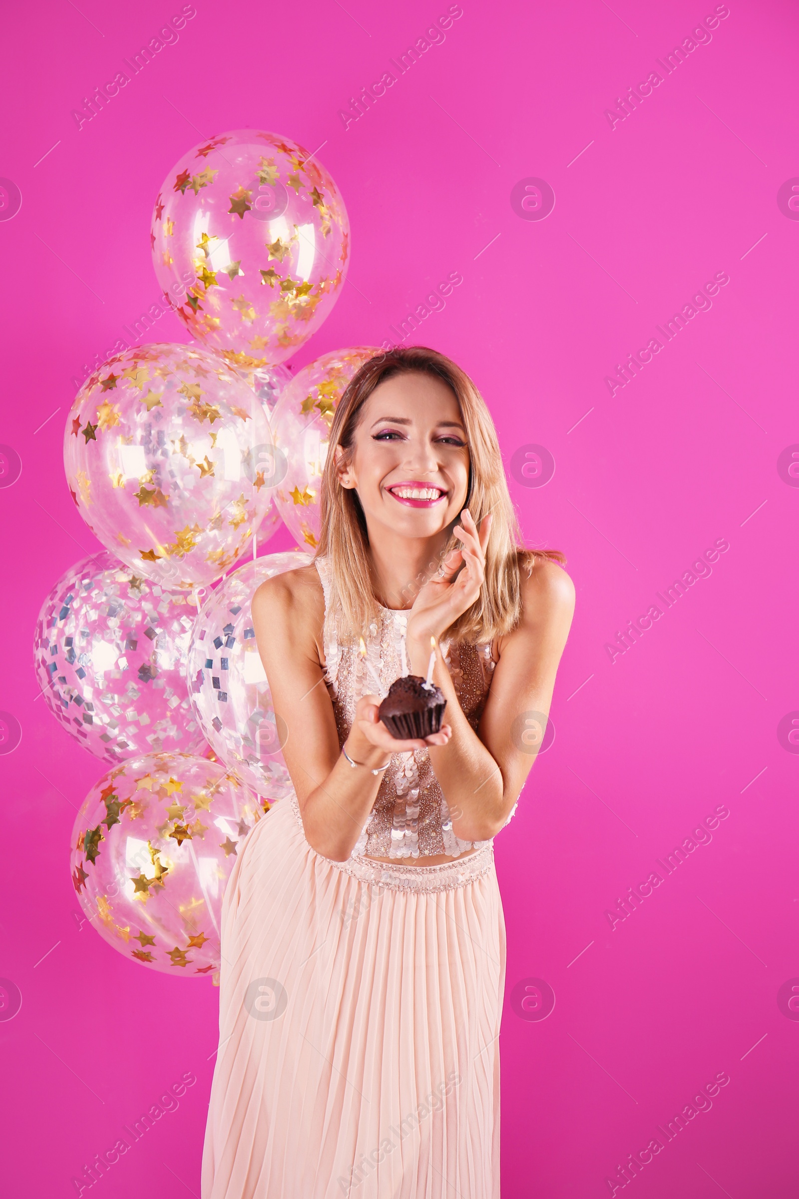 Photo of Young woman with birthday muffin and air balloons on color background