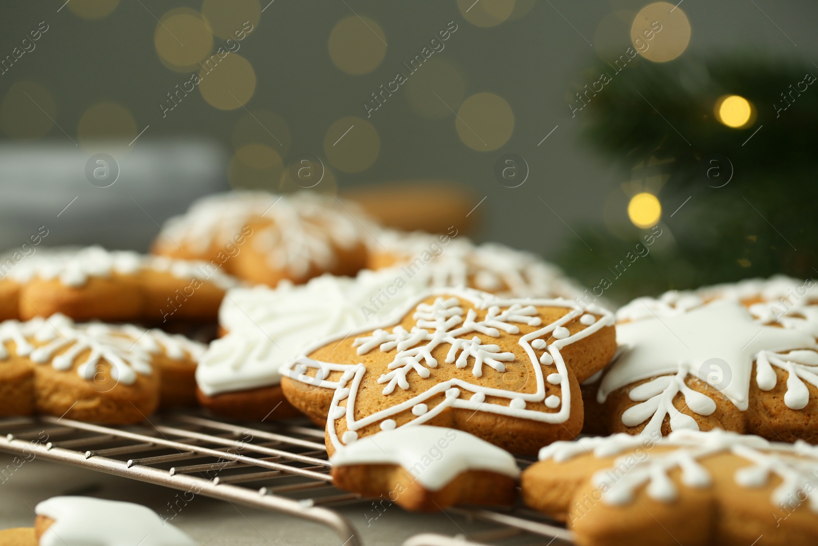 Photo of Tasty Christmas cookies with icing on baking grid against blurred lights, closeup