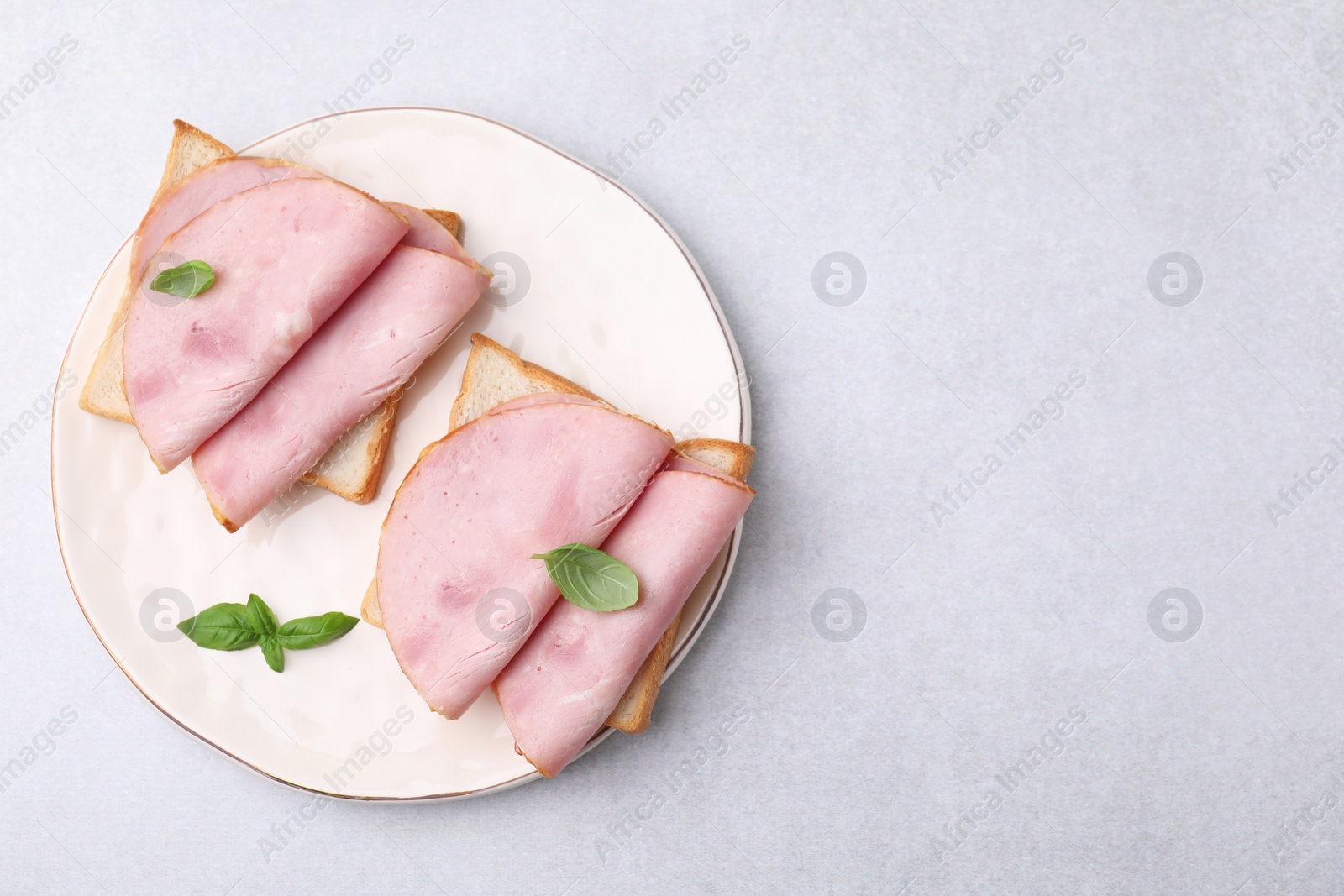 Photo of Delicious sandwiches with ham on light gray table, top view. Space for text