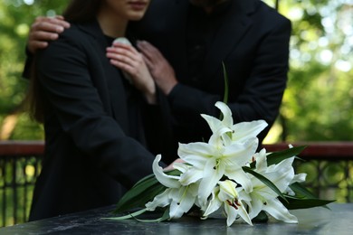 Photo of People near white lilies on tombstone at cemetery, closeup. Funeral ceremony