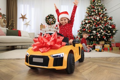 Cute little girl driving toy car in room decorated for Christmas