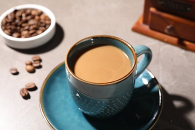 Delicious coffee with milk in cup and beans on light table, closeup