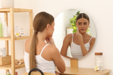 Photo of Beautiful woman removing makeup with cotton pad near mirror at home