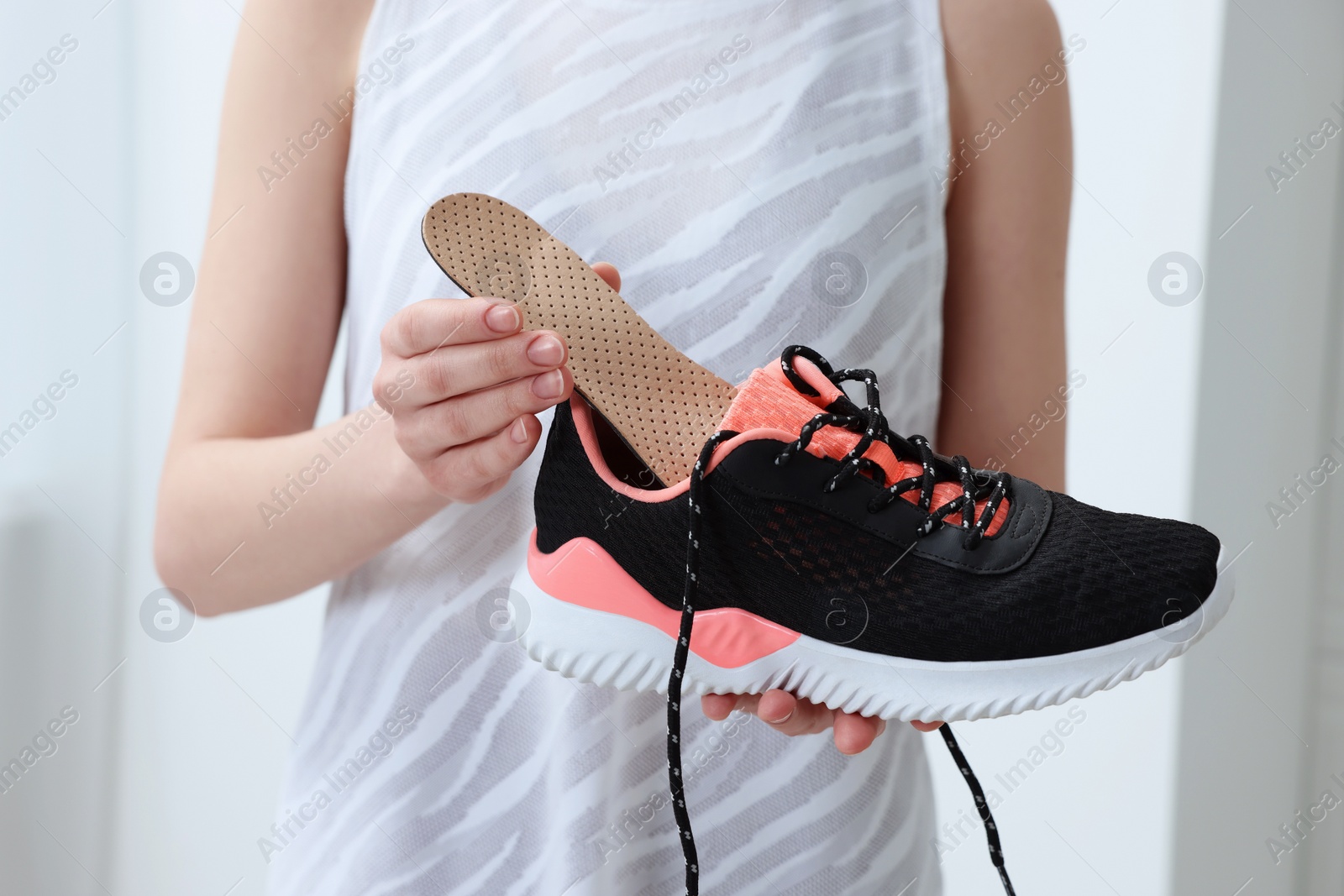 Photo of Woman putting orthopedic insole into shoe indoors, closeup. Foot care