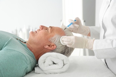 Photo of Senior man with hair loss problem receiving injection in salon