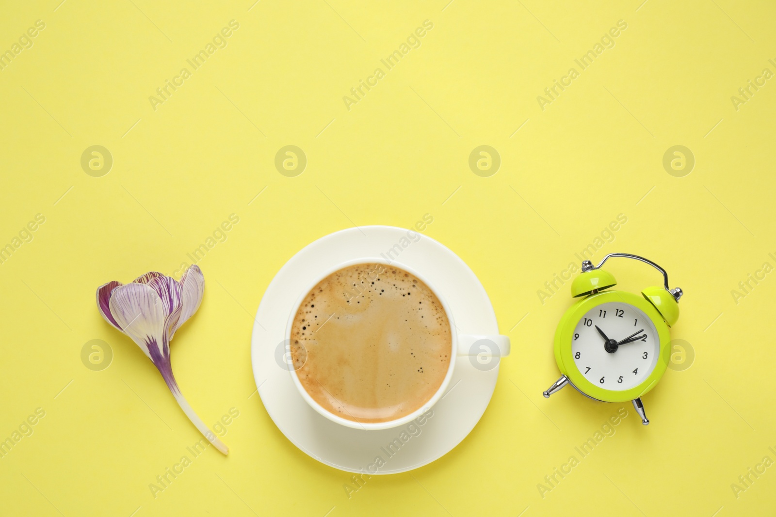 Photo of Delicious morning coffee, alarm clock and flower on yellow background, flat lay. Space for text