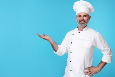 Happy chef in uniform posing on light blue background, space for text