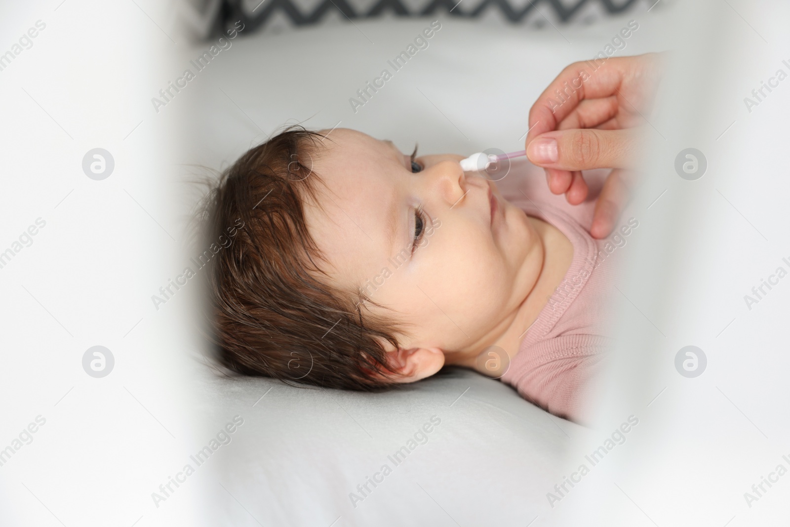 Photo of Mother cleaning nose of her baby with cotton bud on bed, closeup