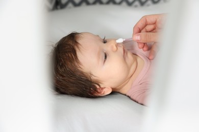 Photo of Mother cleaning nose of her baby with cotton bud on bed, closeup