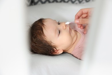 Mother cleaning nose of her baby with cotton bud on bed, closeup