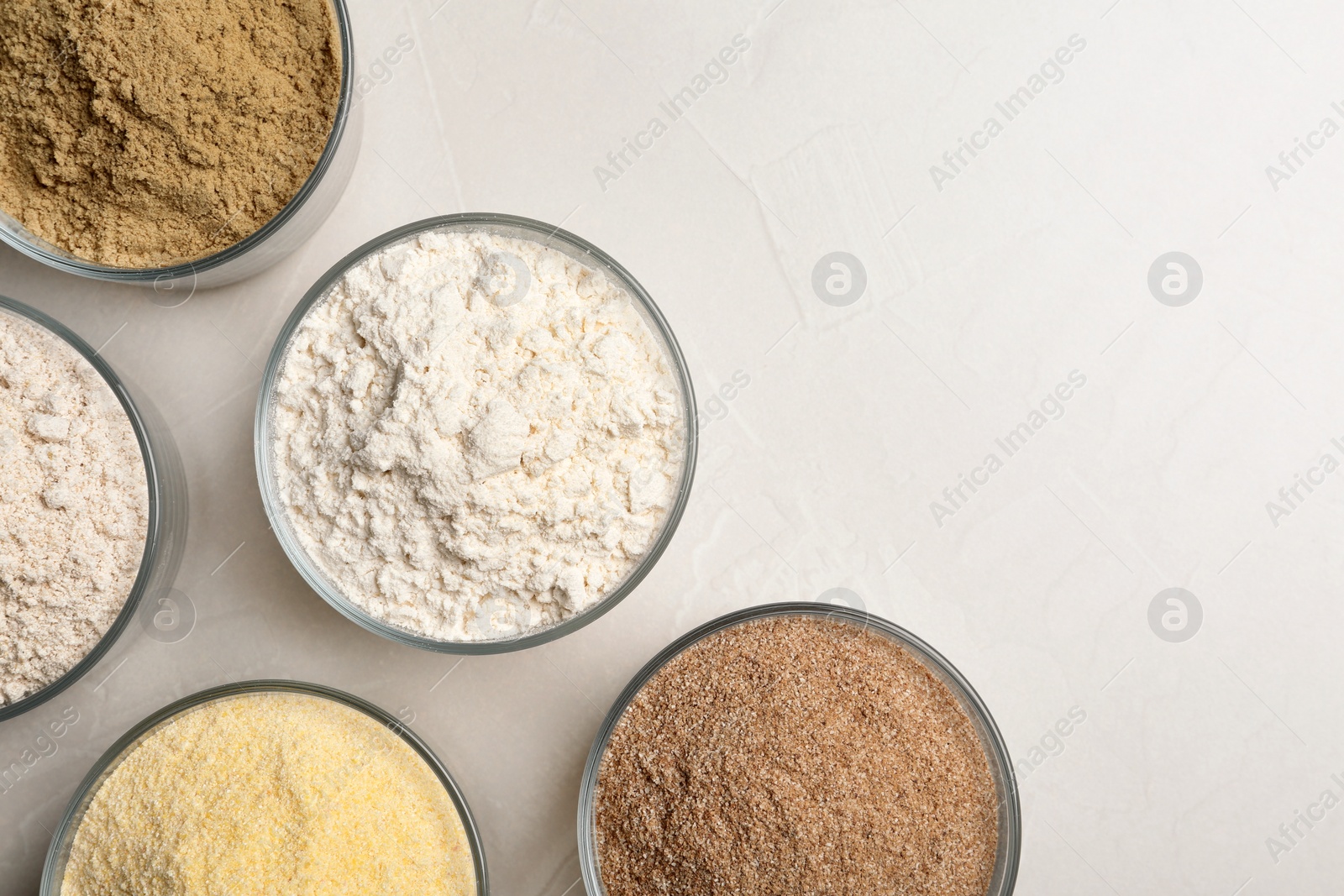 Photo of Bowls with different types of flour on light background, top view. Space for text