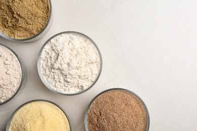 Photo of Bowls with different types of flour on light background, top view. Space for text