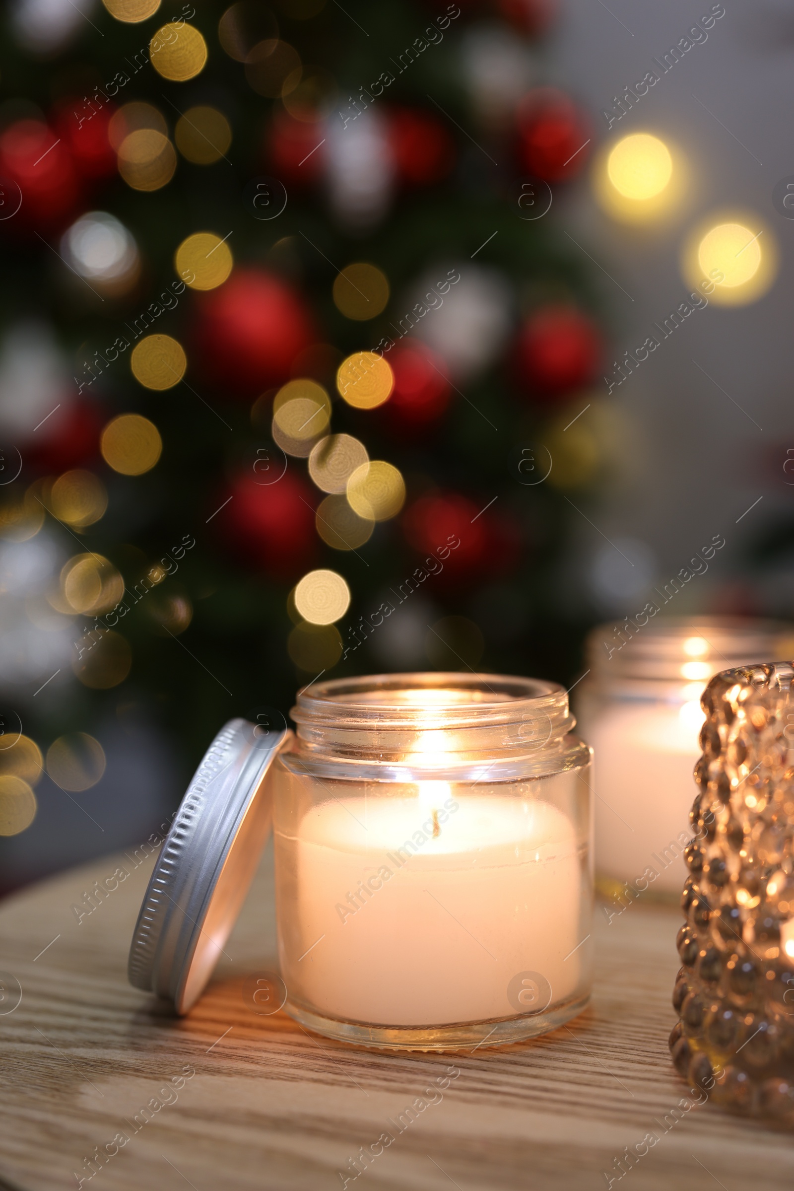 Photo of Burning candles on wooden table in room decorated for Christmas