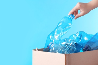 Woman putting used plastic bottle into cardboard box on color background, closeup with space for text. Recycling problem