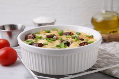 Photo of Tasty sausage casserole with green onion in baking dish on white marble table, closeup