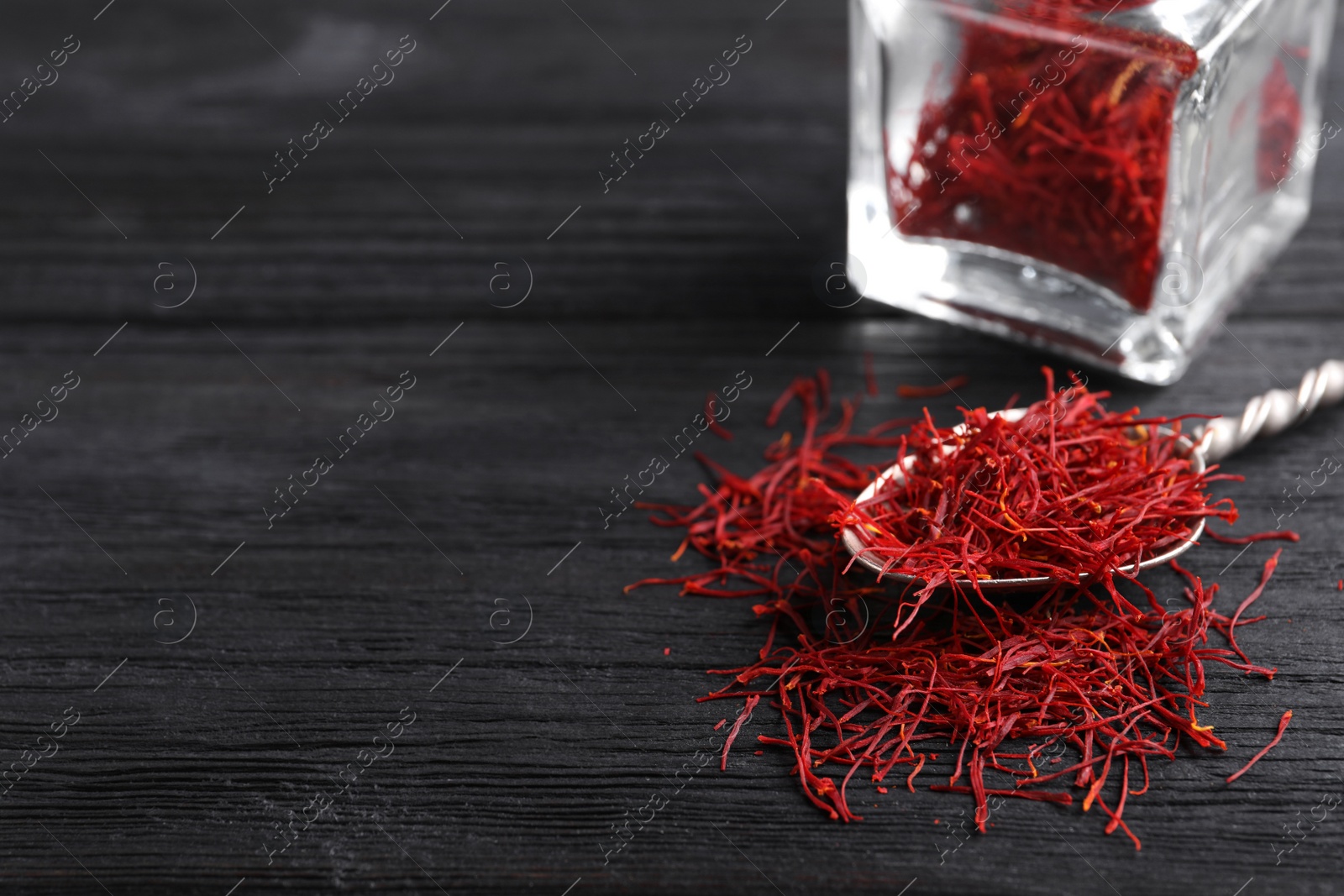 Photo of Dried saffron on black wooden table, closeup. Space for text