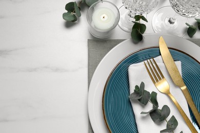 Stylish setting with cutlery and eucalyptus leaves on white marble table, flat lay. Space for text