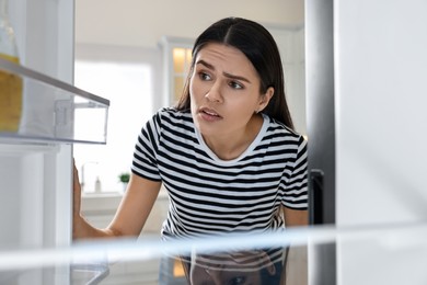 Upset woman near empty refrigerator in kitchen, view from inside