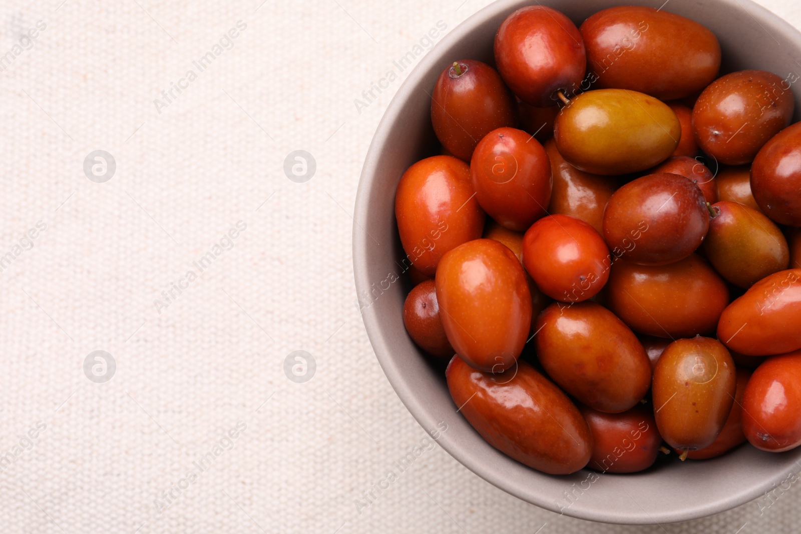 Photo of Fresh Ziziphus jujuba fruits in bowl on white tablecloth, top view. Space for text