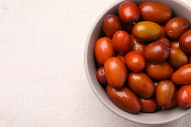 Photo of Fresh Ziziphus jujuba fruits in bowl on white tablecloth, top view. Space for text