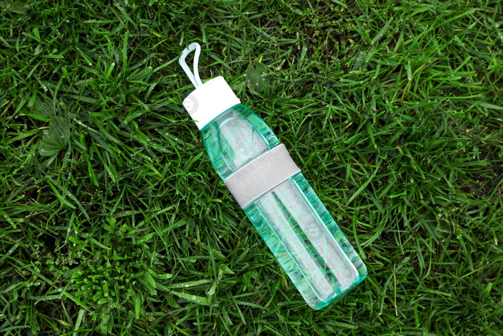 Photo of Glass bottle of fresh water on green grass, top view