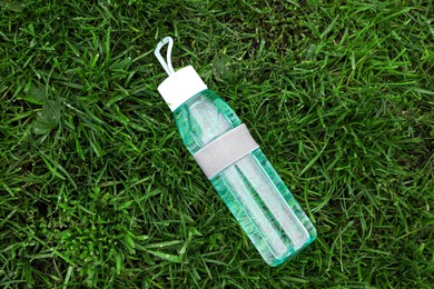 Photo of Glass bottle of fresh water on green grass, top view
