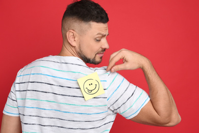Photo of Man with smiling face sticker on back against red background. April fool's day