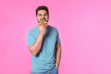 Handsome man with pizza on pink background, space for text