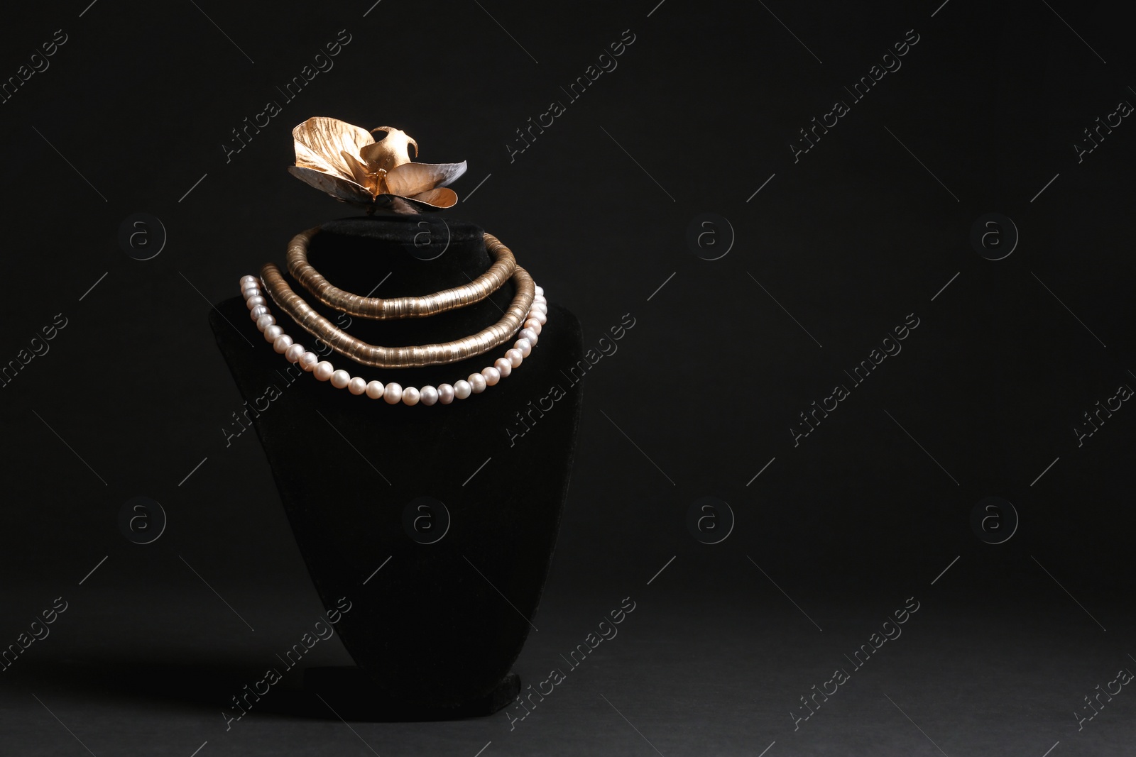 Photo of Stylish necklaces and decorative flower on stand against black background, space for text. Luxury jewelry