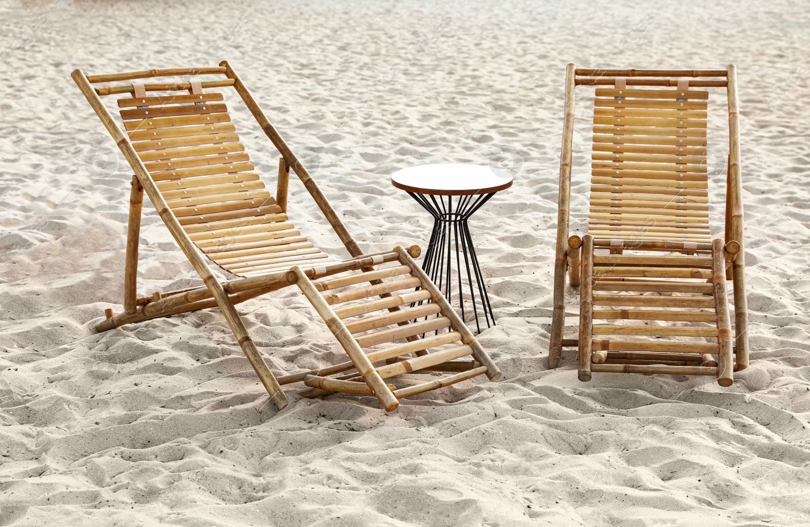 Photo of Empty wooden sunbeds and table on sandy shore. Beach accessories