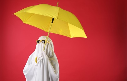 Photo of Person in ghost costume and sunglasses holding yellow umbrella on red background, space for text