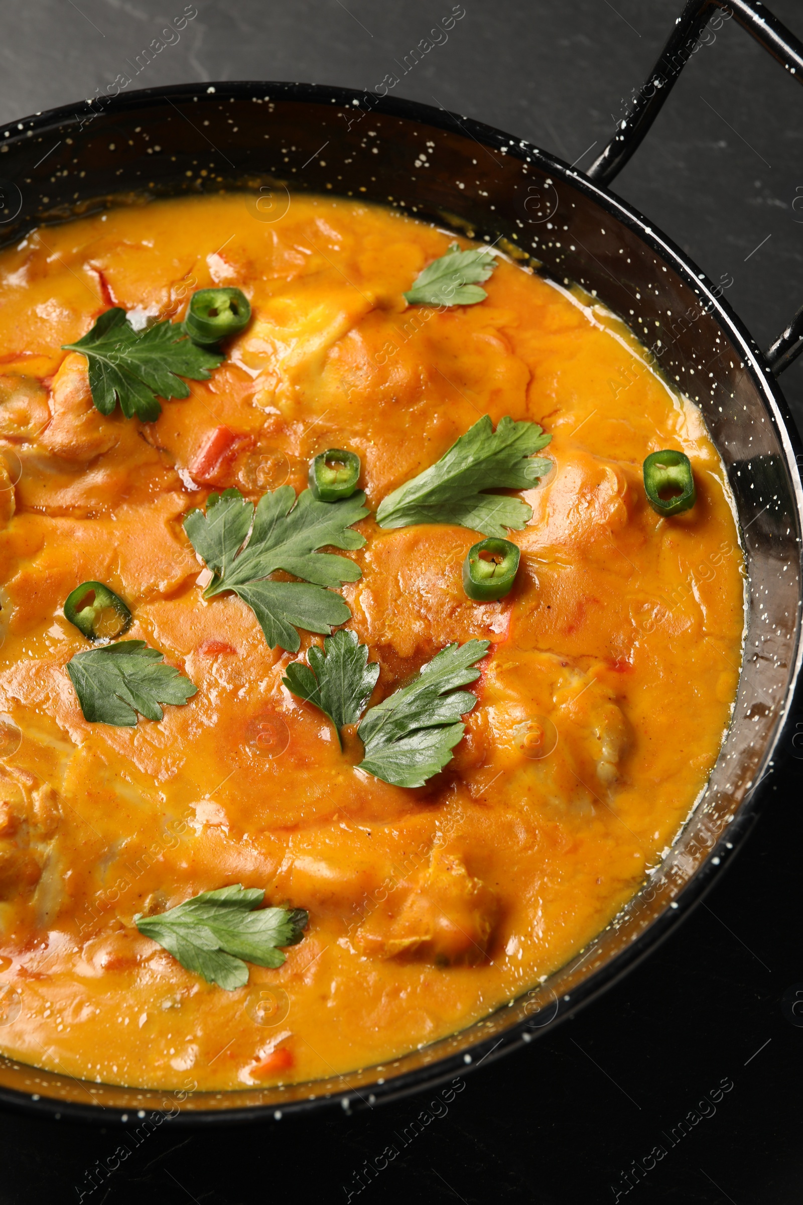 Photo of Tasty chicken curry with parsley and pepper on black table